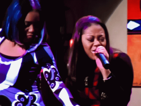 Two Women Singing Into Microphones One In Purple Dress GIF