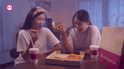 Two Women Sit At A Table With A Box Of Pizza And A Bag That Says Foodpanda GIF
