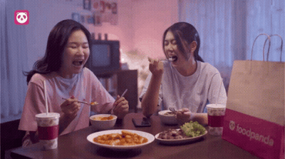 Two Women Sit At A Table With Food And A Bag That Says Foodpanda On It GIF
