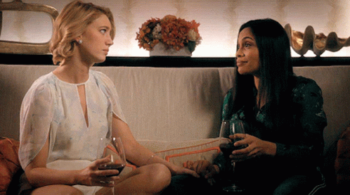 Two Women Sit On A Couch Drinking Wine GIF