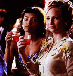 Two Women Sitting At A Table Holding Glasses Of Red Liquid GIF