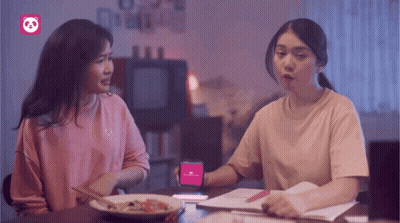 Two Women Sitting At A Table With A Phone That Says ' Panda ' On It GIF