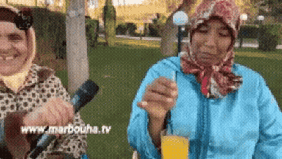 Two Women Sitting In Park With Microphone And Orange Juice GIF