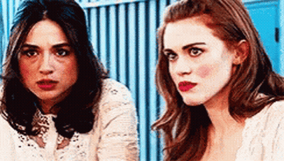 Two Women Sitting Next To Each Other In Front Of Blue Fence GIF