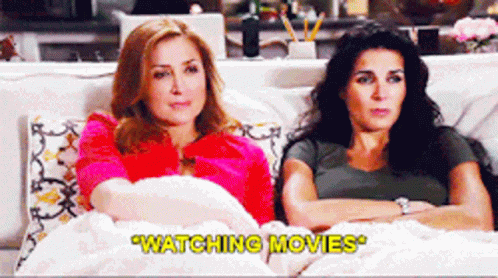 Two Women Sitting On A Couch Watching Movies With The Caption " Watching Movies " GIF