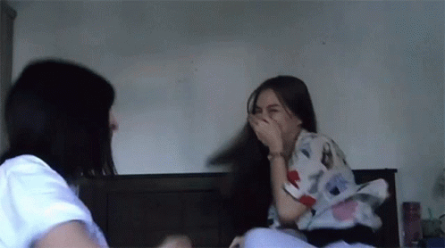 Two Women Sitting On Bed Laughing And Covering Mouths GIF