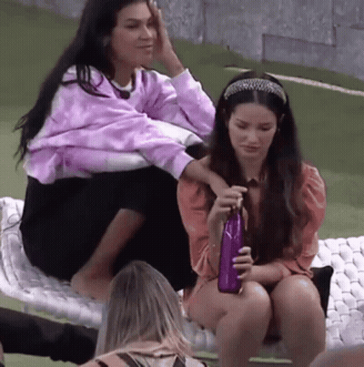 Two Women Sitting on Blanket One Holding Purple Bottle