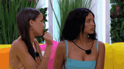 Two Women Sitting On Colorful Couch, One In Blue Top GIF