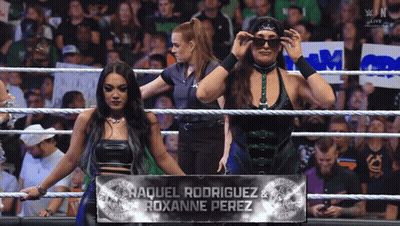Two Women Standing In A Wrestling Ring With A Banner That Says Raquel Rodriguez & Roxanne Perez GIF