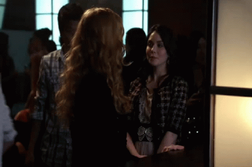 Two Women Standing In Crowded Room Talking GIF