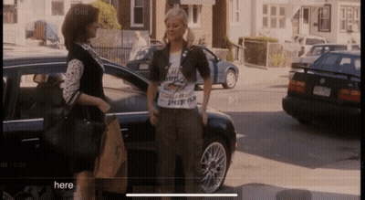 Two Women Standing In Front Of A Car With The Word Here On The Bottom GIF