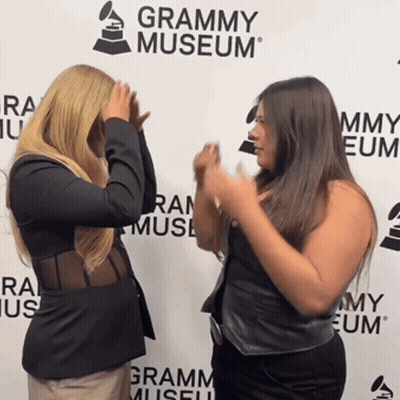 Two Women Standing In Front Of A Grammy Museum Sign GIF