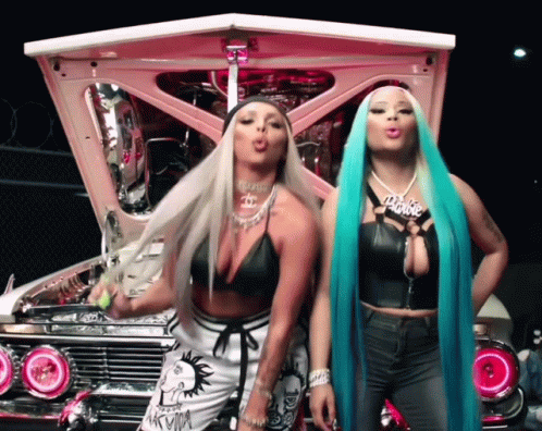 Two Women Standing In Front Of A Pink Car And One Has A Barbie Necklace GIF