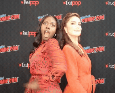 Two Women Standing In Front Of A Wall That Says Comic Con On It GIF