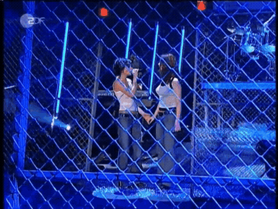 Two Women Standing In Front Of Chain Link Fence GIF