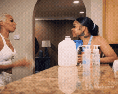 Two Women Standing In Front Of Counter With Gallon Of Milk GIF