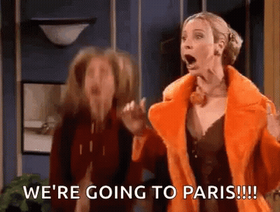 Two Women Standing In Room One In Orange Coat GIF