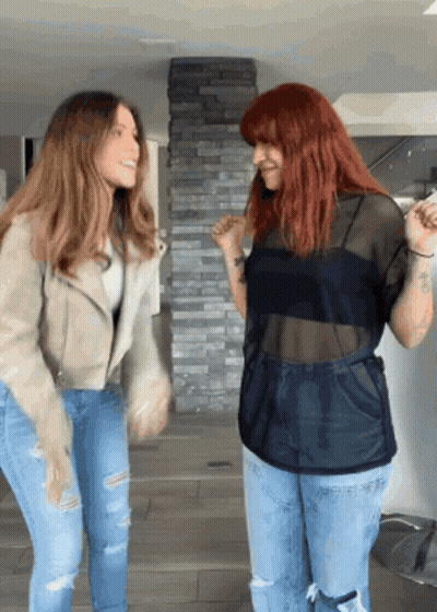Two Women Standing Next To Each Other Dancing In Front Of A Stone Wall GIF