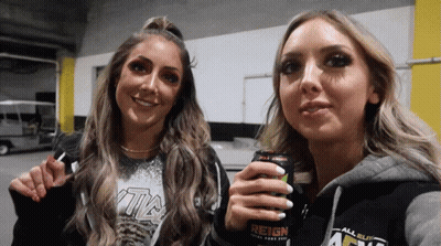 Two Women Standing Next To Each Other Holding A Can Of Reign Energy Drink GIF