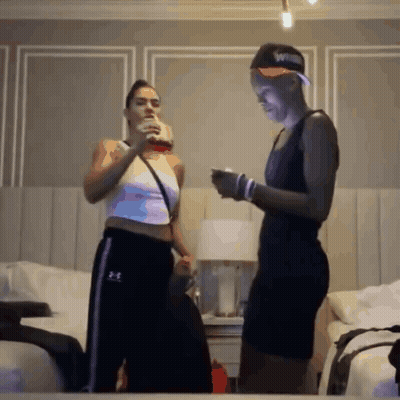 Two Women Standing Next To Each Other In A Bedroom Wearing Under Armour Sweatpants GIF