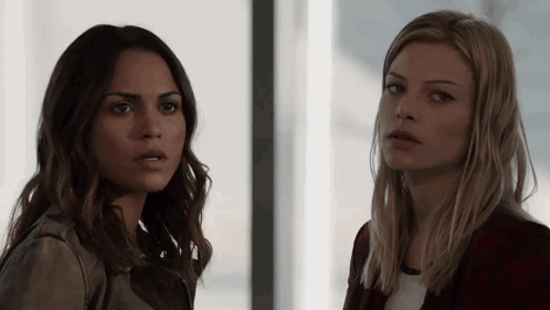 Two Women Standing Next To Each Other Looking At Camera GIF