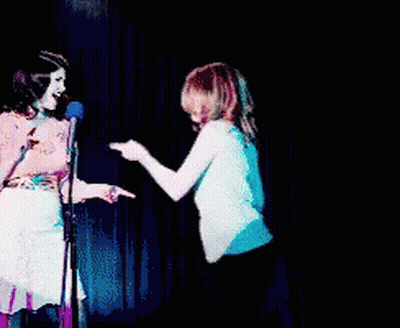 Two Women Standing Next To Each Other On A Stage GIF
