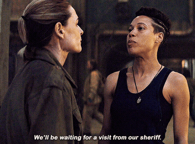 Two Women Standing Next To Each Other Saying We'll Be Waiting For A Visit From Our Sheriff GIF