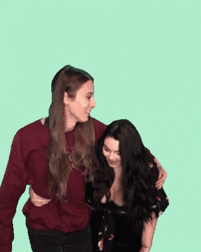 Two Women Standing Next To Each Other With One Wearing A Maroon Sweater GIF