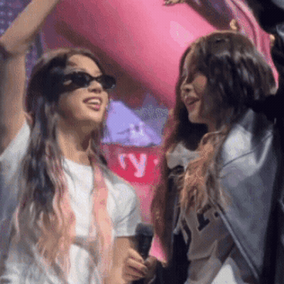 Two Women Standing Next To Each Other With One Wearing Sunglasses And Holding A Microphone GIF