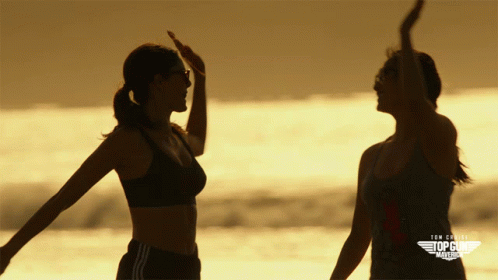 Two Women Standing On A Beach With The Words Top Gun America On The Bottom Right GIF