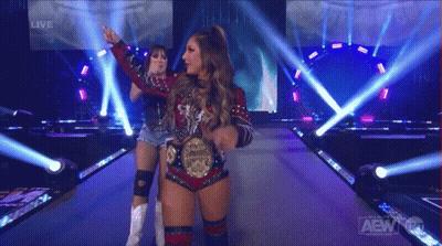Two Women Standing On Stage With AEW Logo GIF
