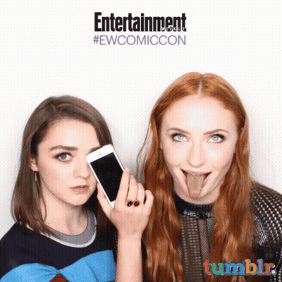 Two Women Sticking Their Tongues Out In Front Of A Sign That Says Entertainment #Ewcomiccon GIF