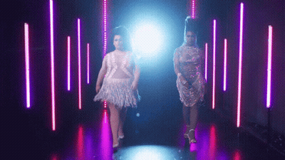 Two Women Walking In Dark Purple-Lit Room GIF
