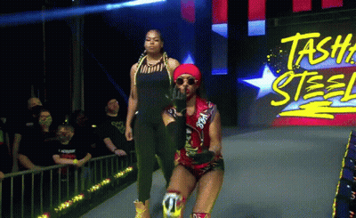 Two Women Walking On Stage With Stash Steel Sign GIF