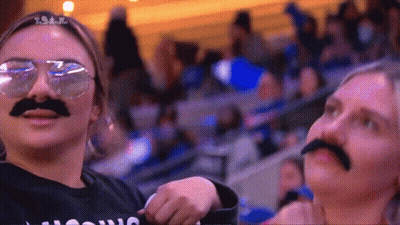 Two Women Wearing Fake Mustaches And Sunglasses Are Standing In A Crowd .. GIF