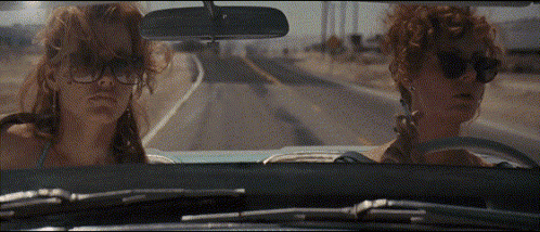 Two Women Wearing Sunglasses Are Driving Down A Road In A Car GIF