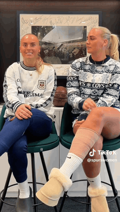 Two Women Wearing Sweaters That Say Coy 'S Are Sitting On Stools GIF