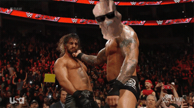 Two Wrestlers Are Dancing In Front Of A Crowd And A Sign That Says Raw GIF