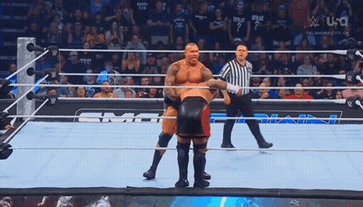 Two Wrestlers Are In A Wrestling Ring With A Referee Standing Behind Them GIF