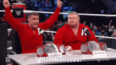 Two Wrestlers Are Sitting At A Table With Their Arms In The Air And One Of Them Is Saying A Thank You GIF