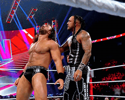 Two Wrestlers Are Standing In A Ring And One Of Them Is Wearing A Black And White Outfit With The Word Wwe On It GIF