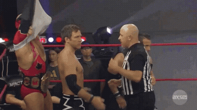 Two Wrestlers Are Standing In A Ring With A Referee In Front Of Them And The Referee Is Wearing An Axs Uniform GIF