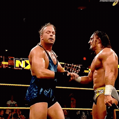 Two Wrestlers Are Standing In A Ring With Their Arms In The Air In Front Of A Sign That Says Nxt GIF