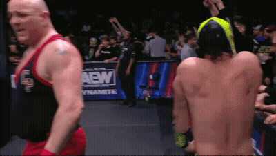Two Wrestlers Are Standing In Front Of A Aew Dynamite Sign GIF