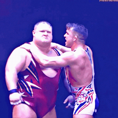 Two Wrestlers Are Standing Next To Each Other And One Of Them Is Wearing A Red And Gold Wrestling Outfit GIF