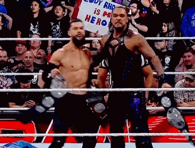 Two Wrestlers Are Standing Next To Each Other In A Wrestling Ring Holding A Sign . GIF