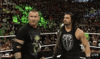 Two Wrestlers Are Standing Next To Each Other In A Wrestling Ring With A Crowd In The Background . GIF