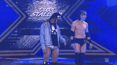 Two Wrestlers Are Standing On A Stage In Front Of A Sign That Says Carl 'S Street GIF