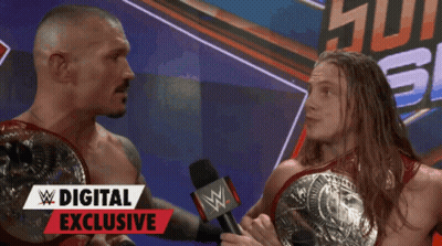 Two Wrestlers Are Talking In Front Of A Digital Exclusive Banner GIF