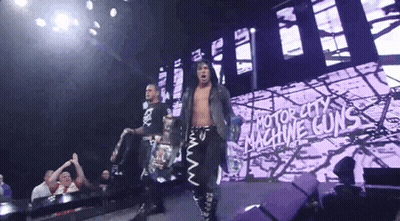 Two Wrestlers Are Walking Down A Stage With A Sign That Says Motor City Machine Guns GIF